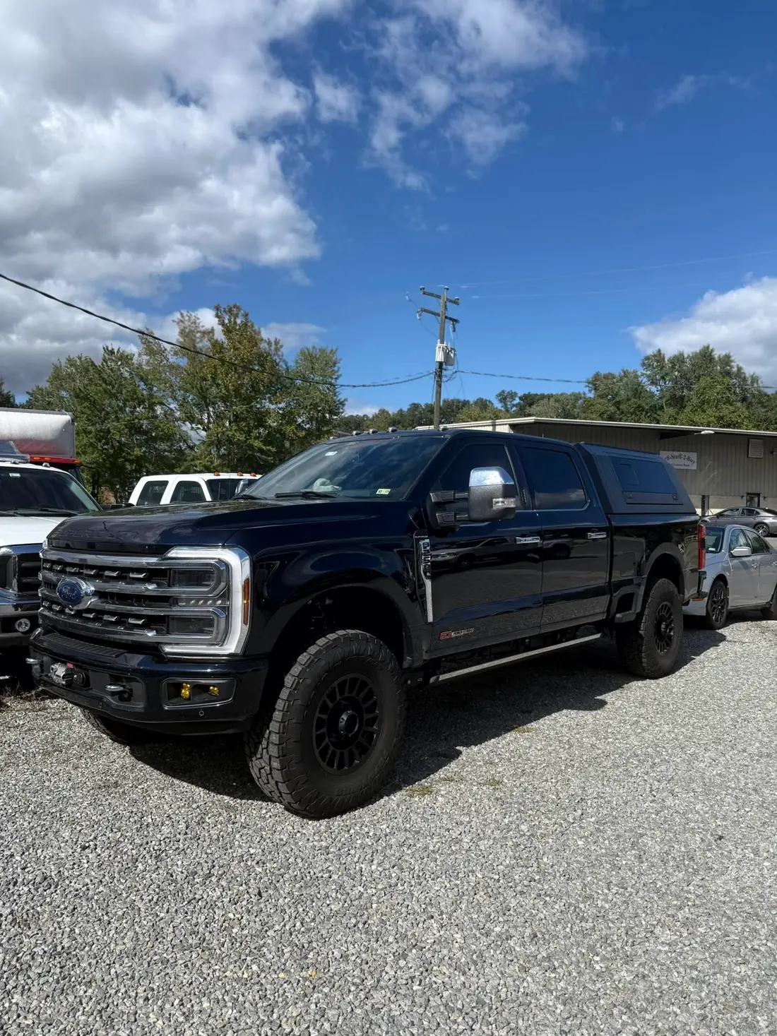 Blue Ford Super Duty with a camper shell outside the shop