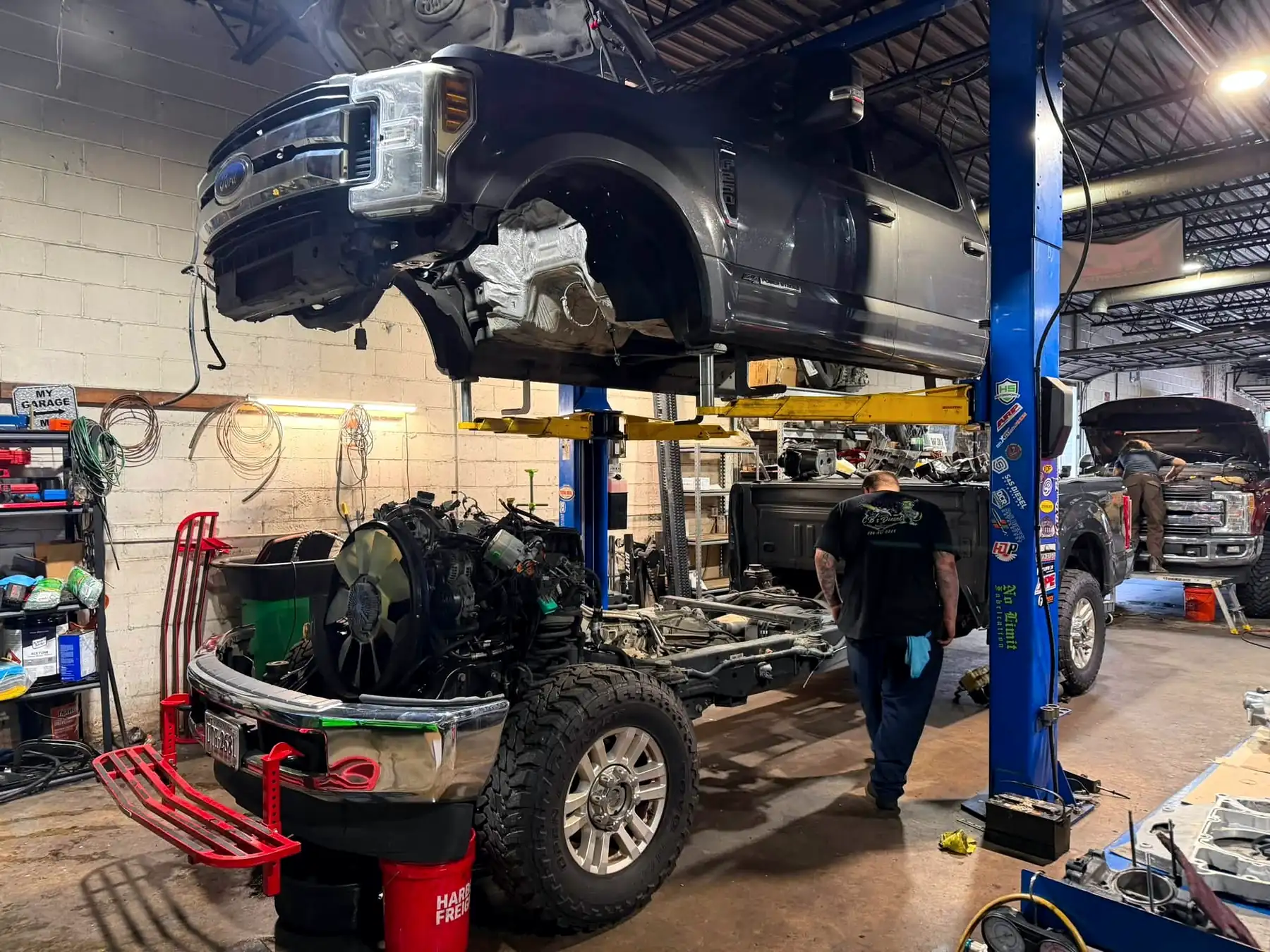 Ford Super Duty raised on a two-post lift with the cab removed, technician working on the bare chassis in the CBS Diesel shop