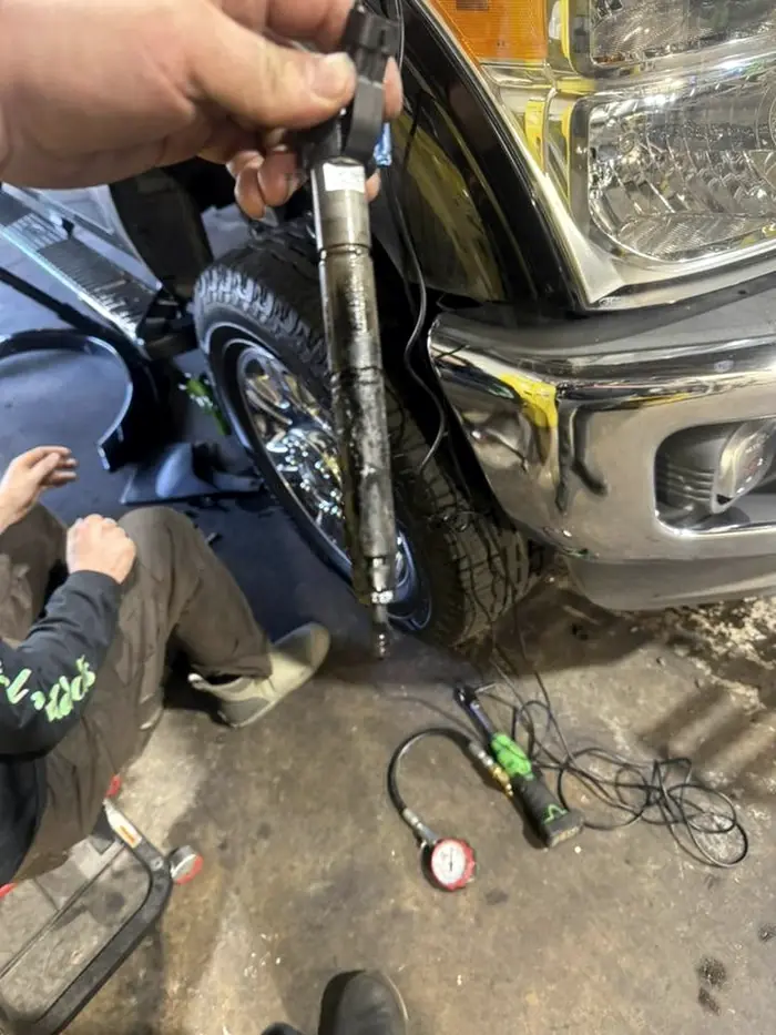 CBS Diesel technician kneeling beside a truck holding a diesel fuel injector