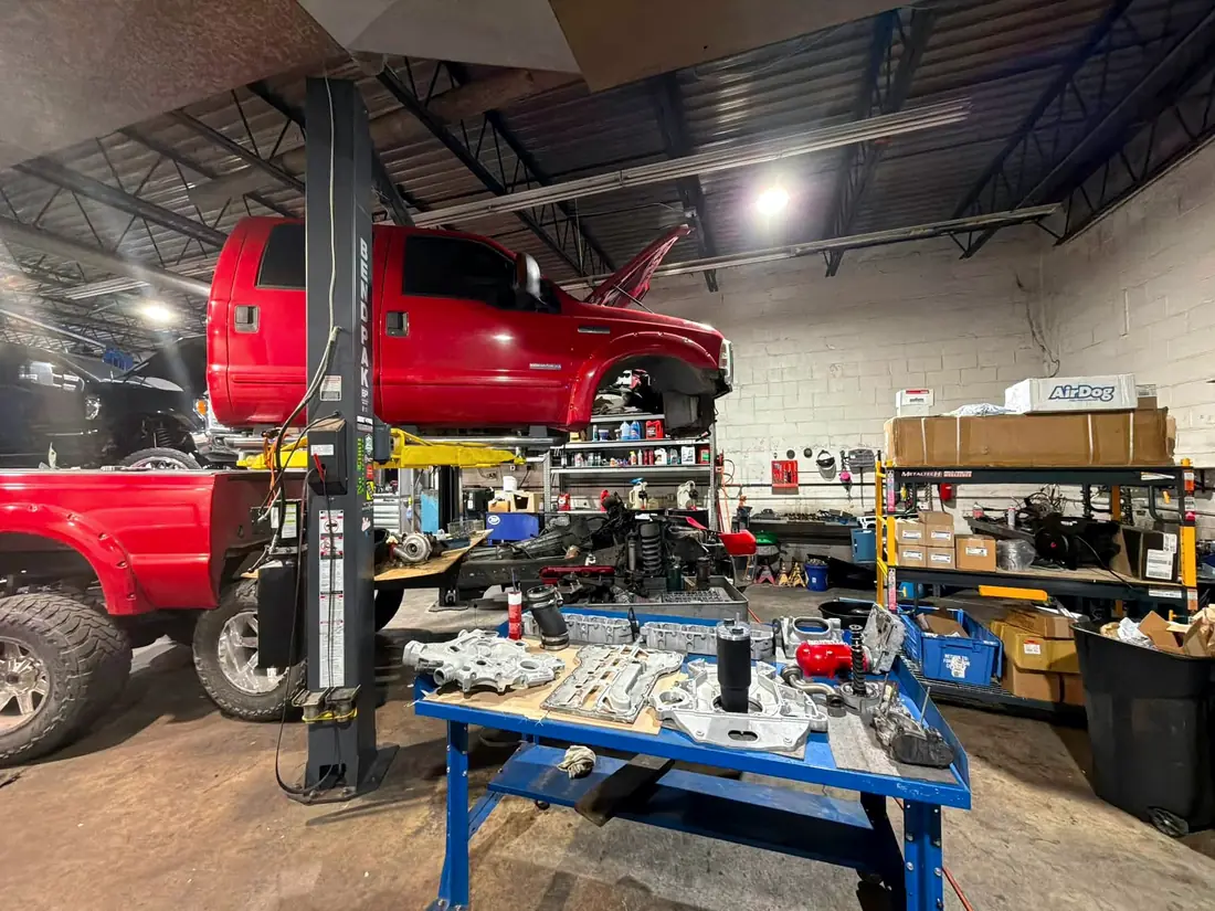 Red Ford Super Duty on the lift with parts laid out across the workbench