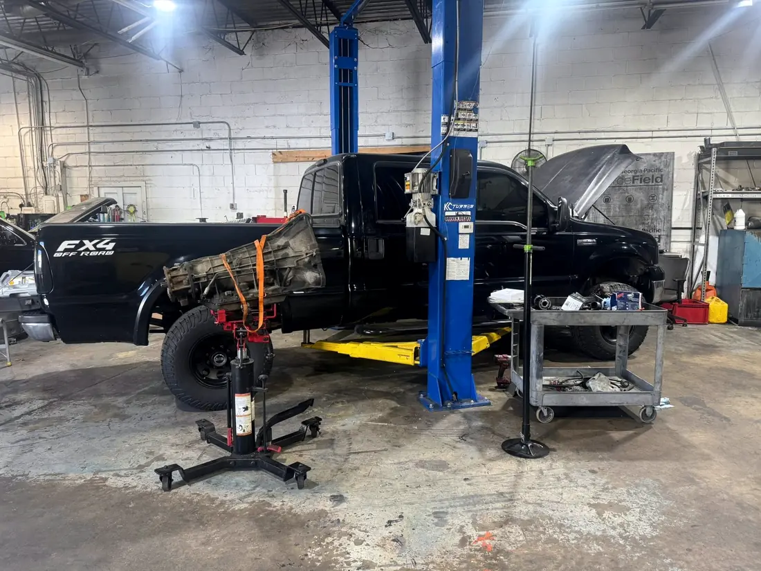 Black Ford Super Duty in the bay with a transmission jack alongside