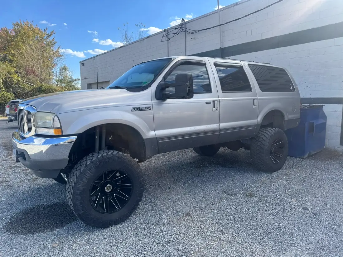 Silver Ford Excursion on aftermarket wheels outside the shop