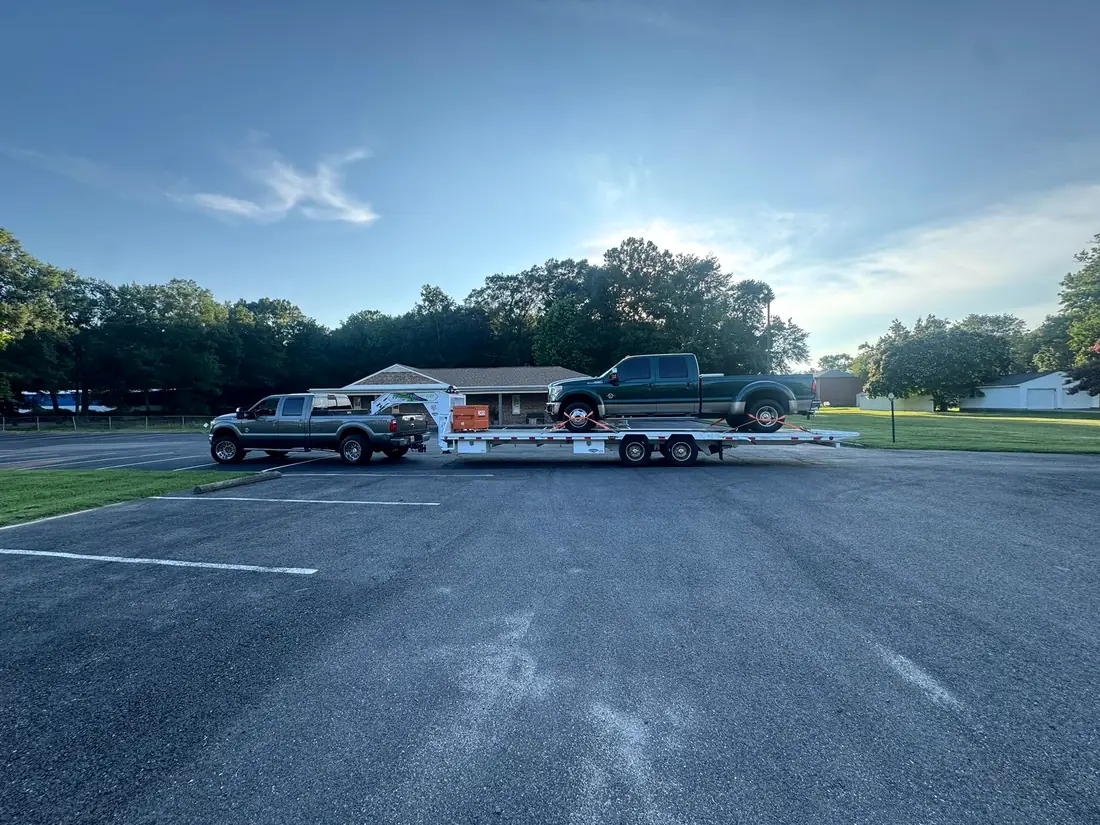 Two diesel pickups loaded on a trailer outside the shop