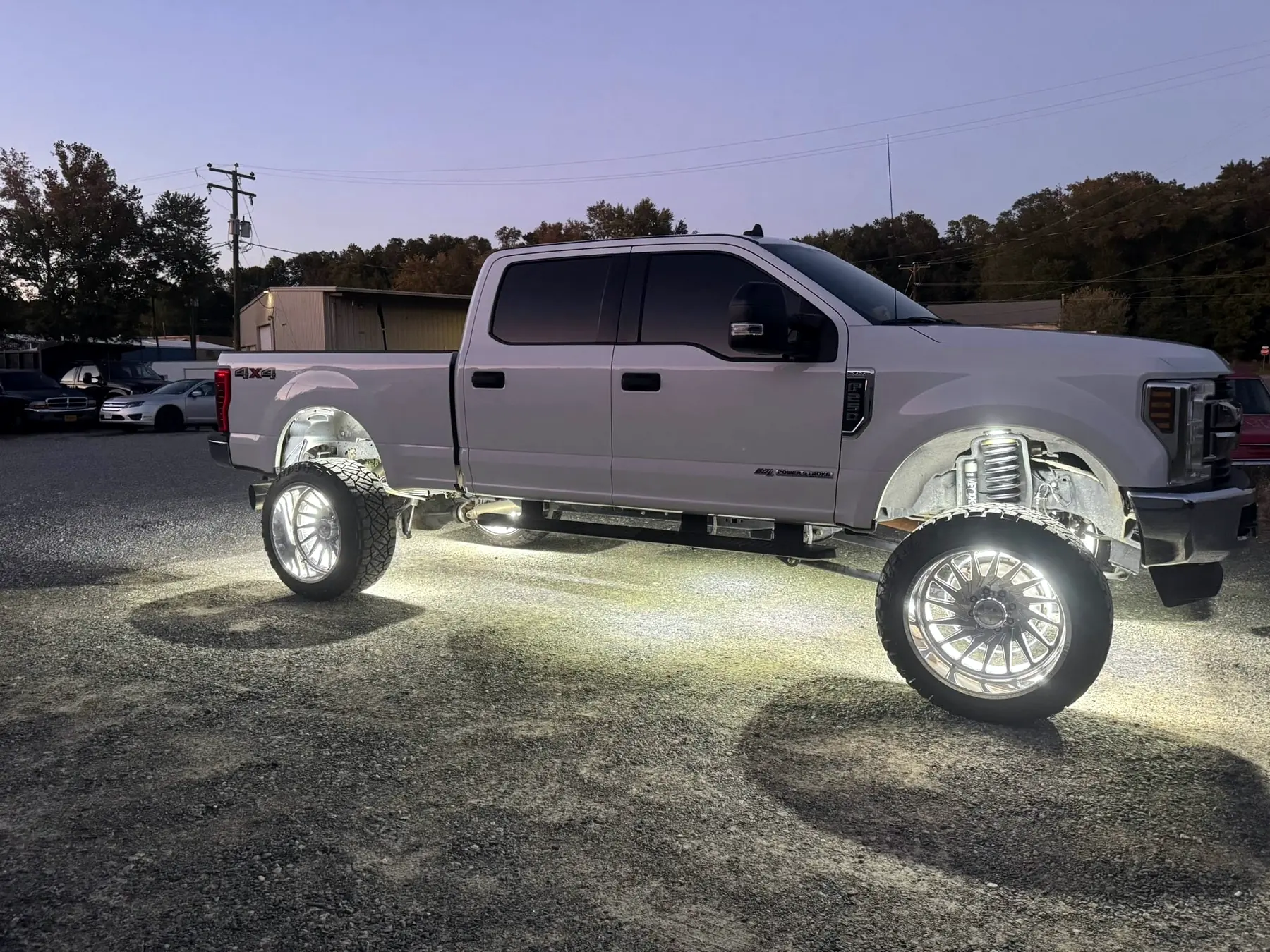 Ford Super Duty on polished aftermarket wheels with underglow, photographed at dusk